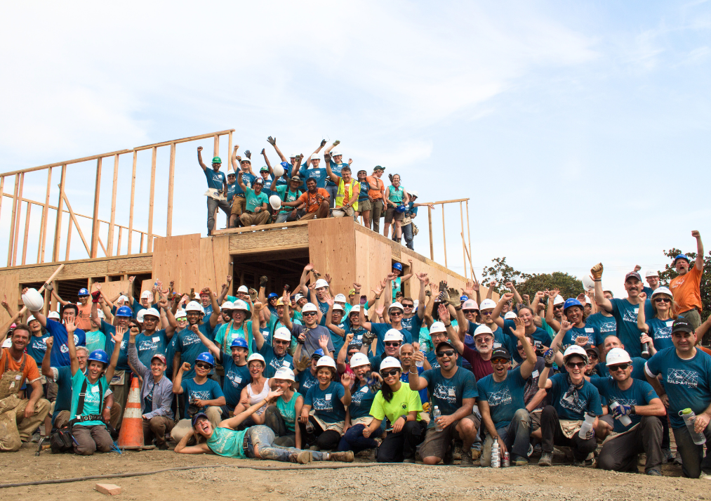  A group photo of many Habitat for Humanity volunteers in front of a framed home.