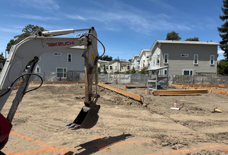 foreground: digger and foundation forms, background: the completed homes of Esperanza Place phase 1
