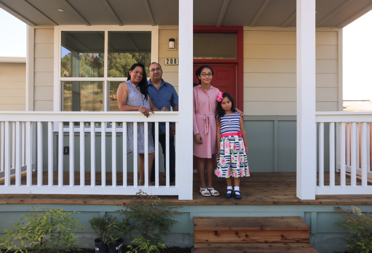 Habitat family of mother, father, and two daughters on front porch of home