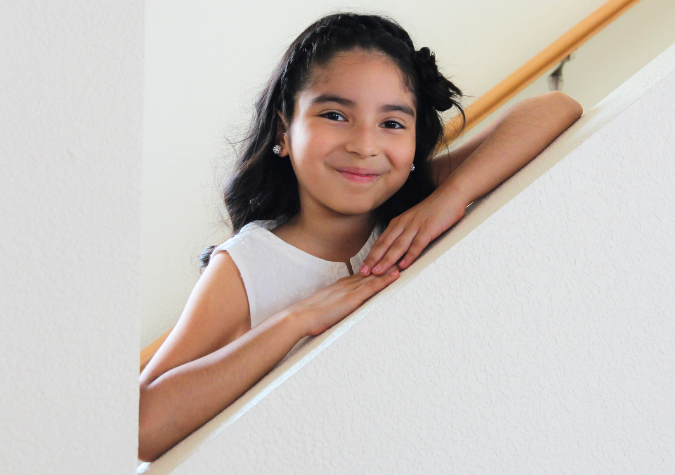 Little girl smiling on the interior stairs of her home.